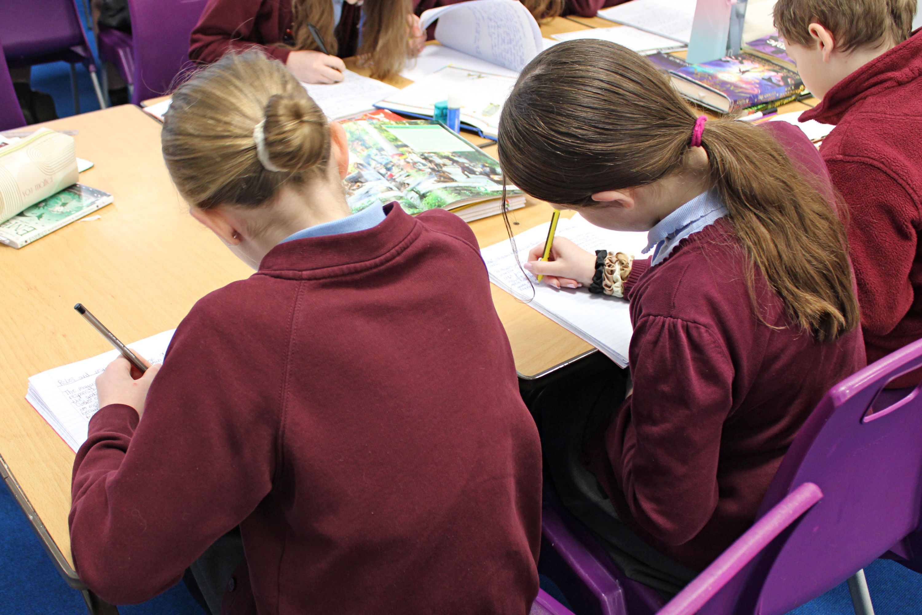 Girls sat next to each other at a desk writing in work books.