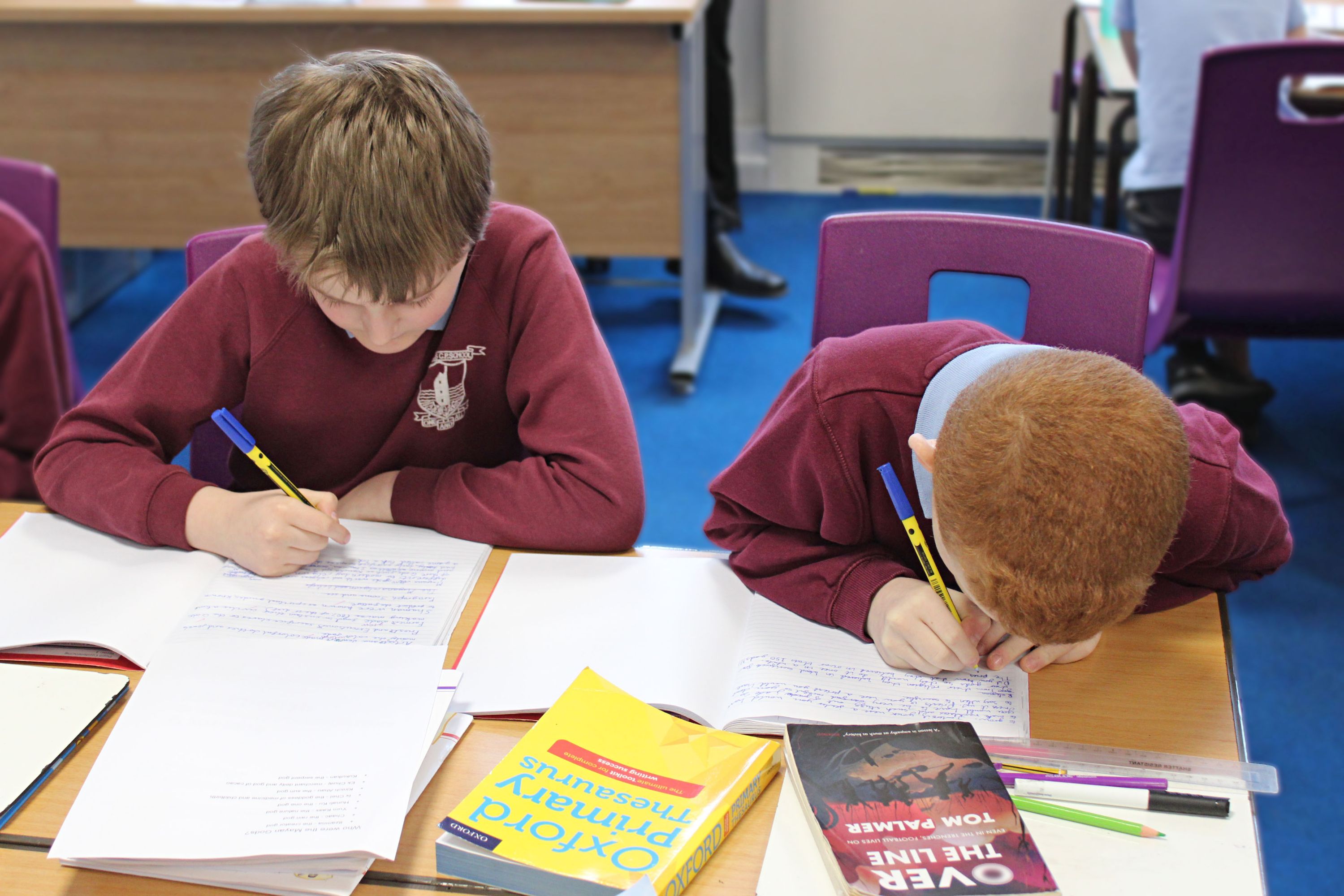 Boys sat next to each other at a desk writing in work books